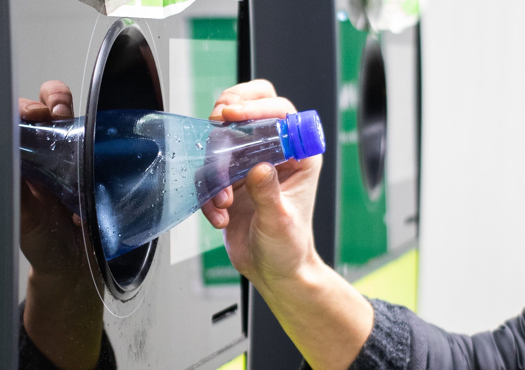 A hand feeding a plastic bottle into a reverse vending machine.